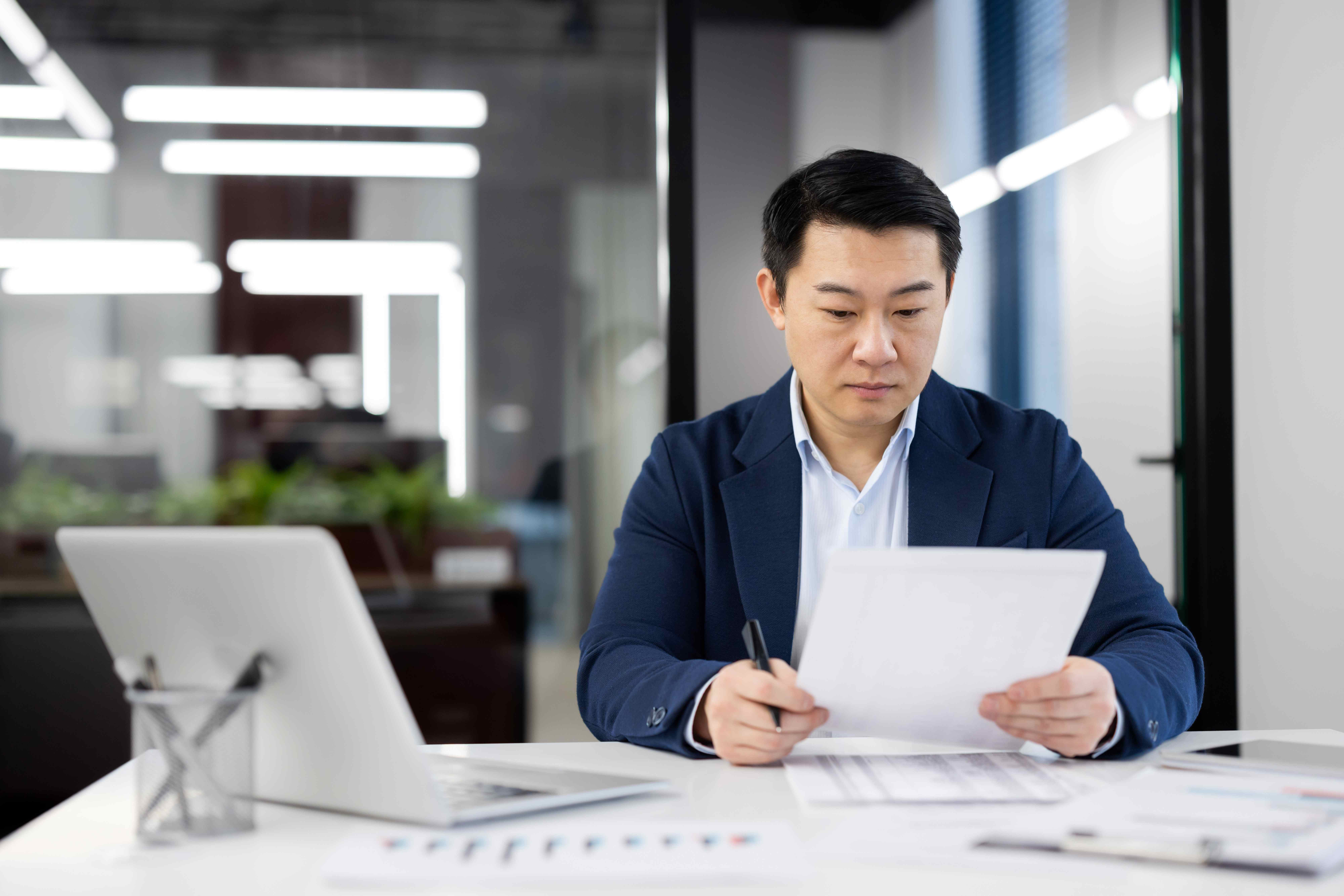 Confident businessman in navy suit reviewing documents and analyzing data in modern office setting