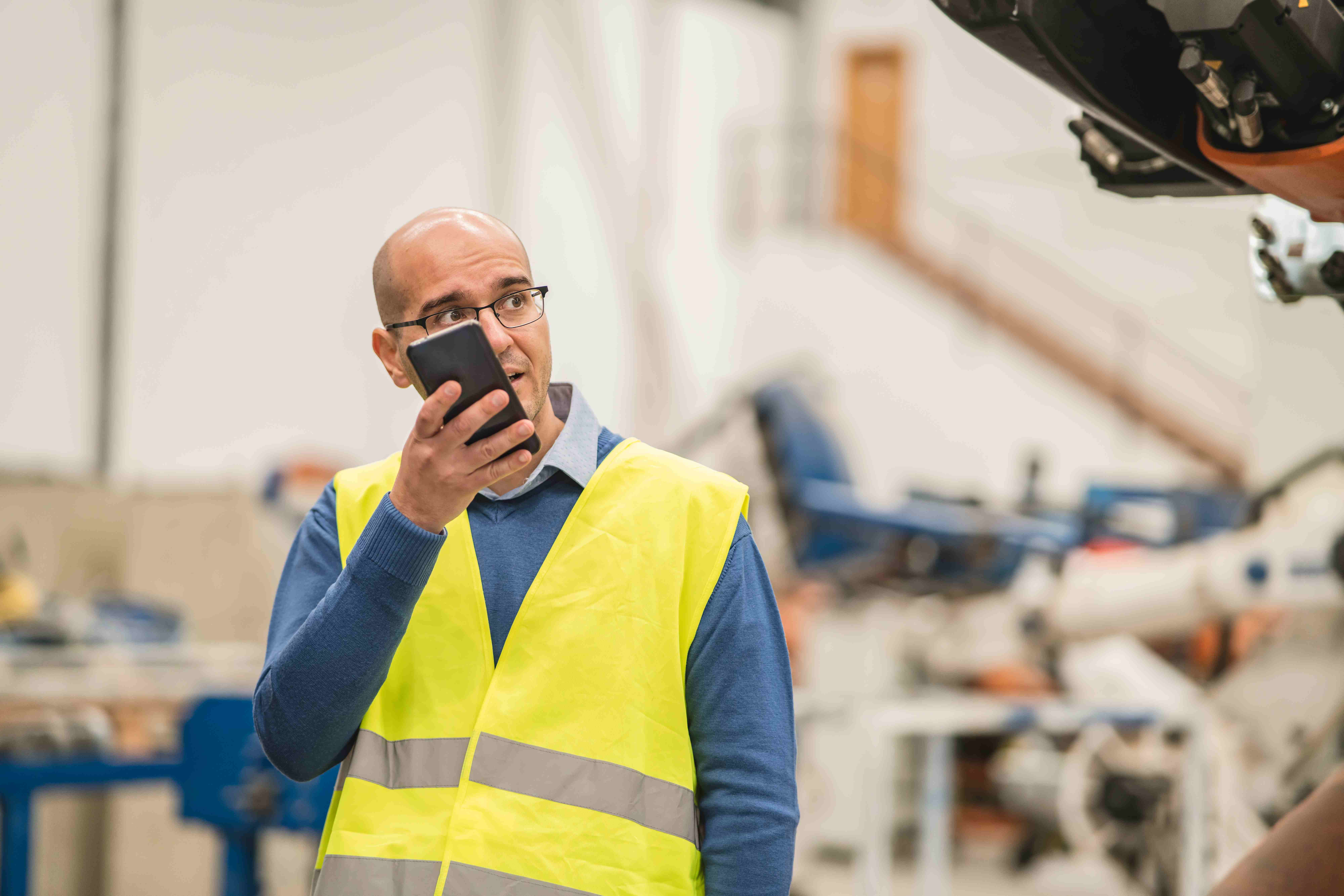 Factory worker in safety vest talking on smartphone in industrial warehouse setting